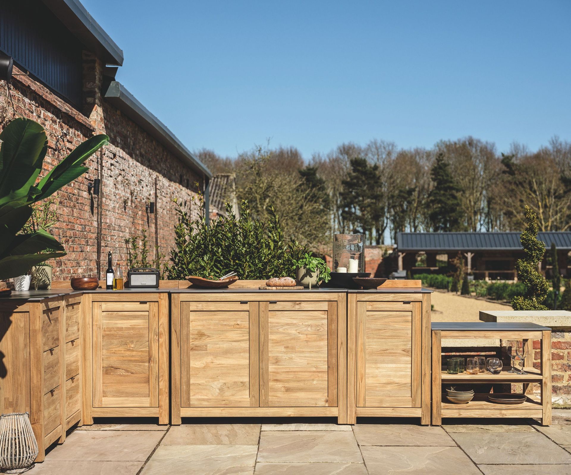 An outdoor kitchen with wooden cabinets, dark gray countertops, and decorated with pretty kitchenware