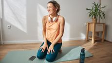 Woman setting up for dead bug exercise on yoga mat, smiling with headphones and water bottle