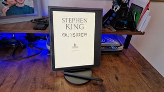 A Kindle Scribe propped up on a desk in front of blue lighting