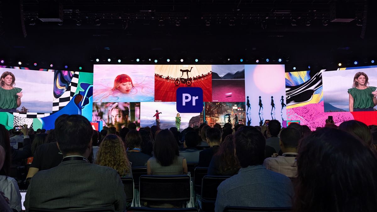 People sitting watching a presentation on large screens displaying a series of images with a large Adobe Premiere Pro logo 