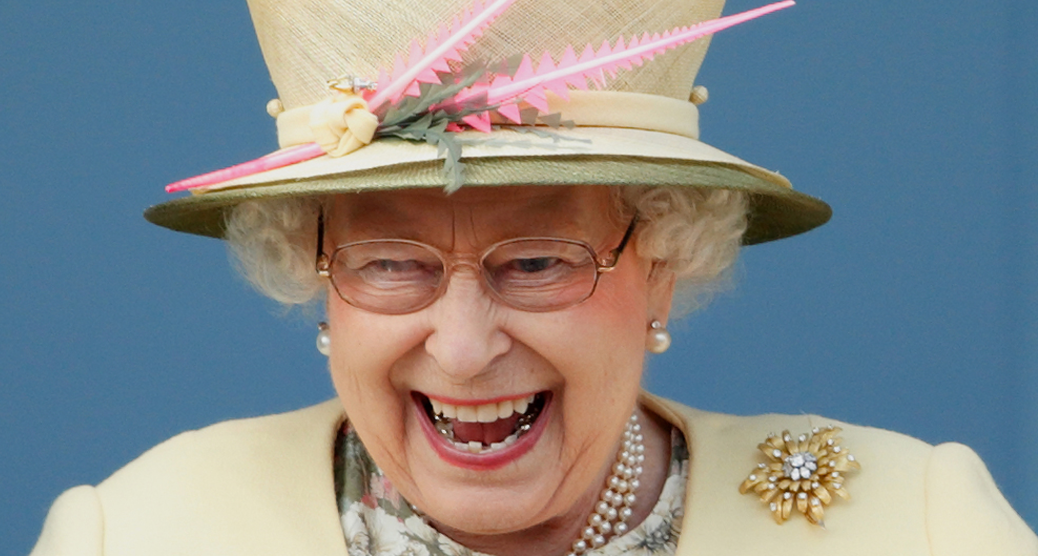 Queen Elizabeth wearing a yellow hat and coat laughing