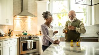 Senior couple stood in their kitchen taking vitamins