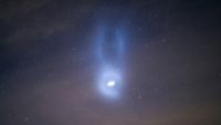 A spiral of light in the night sky with two horn-like pillars of light surrounding it