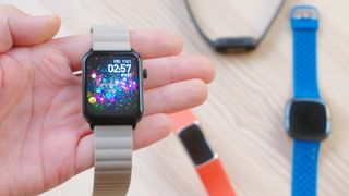 Close-up of the Armitron Matrix in a user&#039;s hand with several out of focus Fitbits on the table in the distance