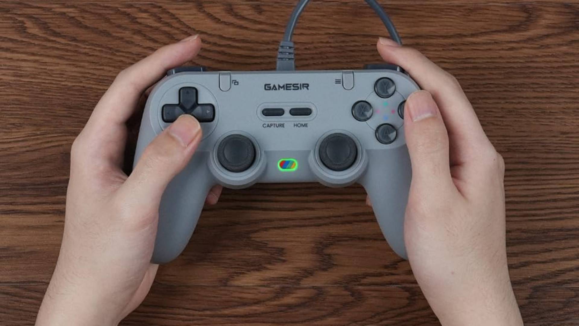 Hands holding GameSir Tegenaria Lite on woodgrain surface.