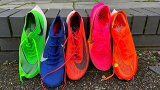 Five models of Nike Vaporfly shoes in a line propped up on a kerb