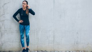 Woman standing against a wall with workout clothes on and headphones, representing exercise snacking ideas