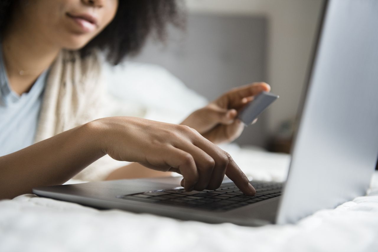 African American woman laying in bed online shopping with laptop 