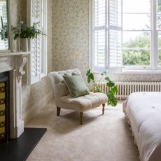 Beige bedroom with cream carpets, floral green and cream wallpaper, and a cream accent chair