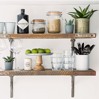 worn wooden shelves fixed to white kitchen wall with small succulents in clay pots and cutlery in white painted tin on display