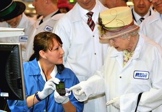 Queen Elizabeth II, wearing a white protective coat (R), is shown a new product, at the final testing before packaging test area during her tour of the RIM (Research In Motion) factory that produces the Blackberry mobile communications handset