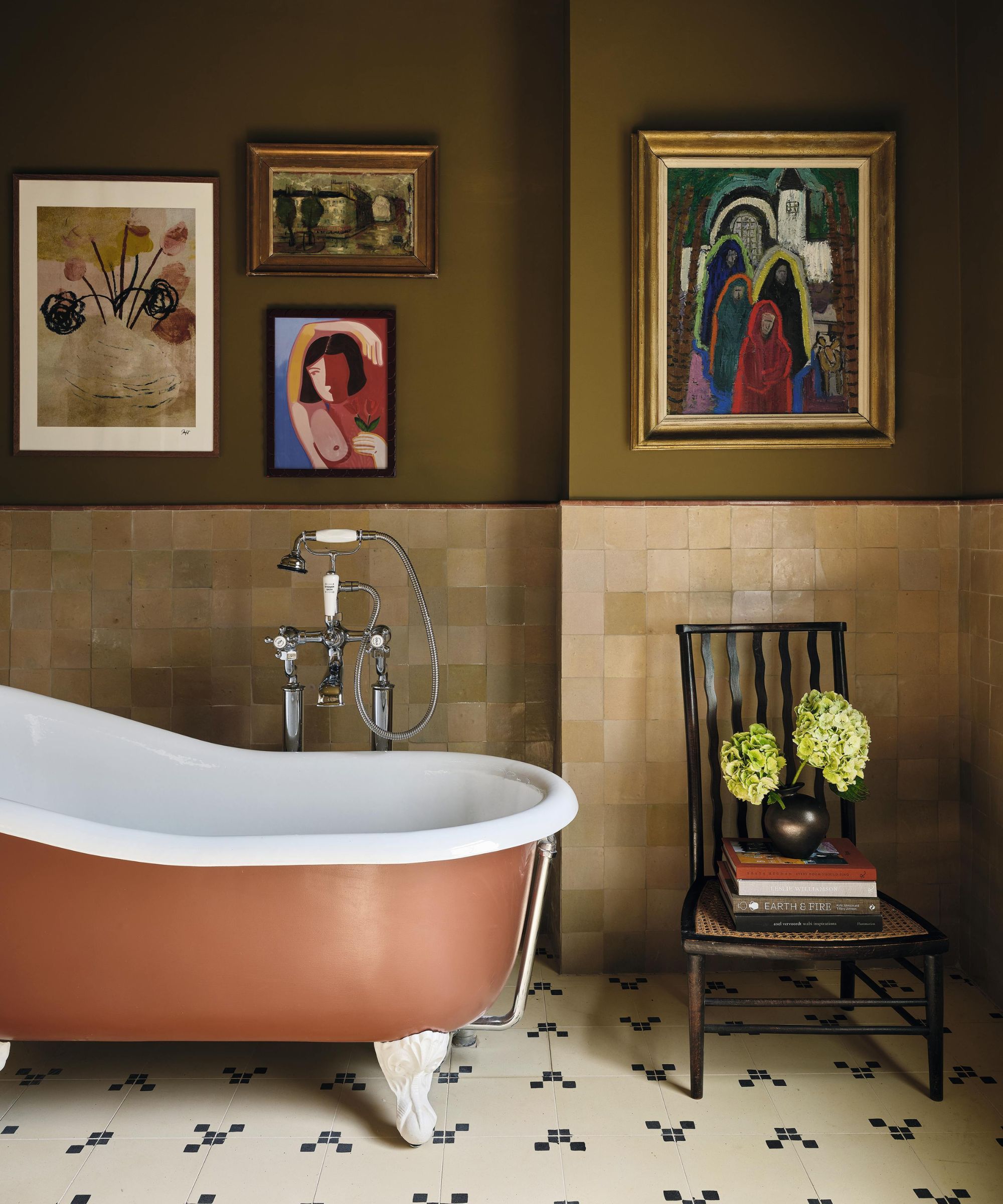 an earthy green bathrom with zellige half height tiles, tiled floor, a rust painted freestanding tub and statement art