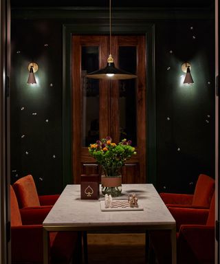 A dark game room with a marble table, green walls, and orange velvet chairs