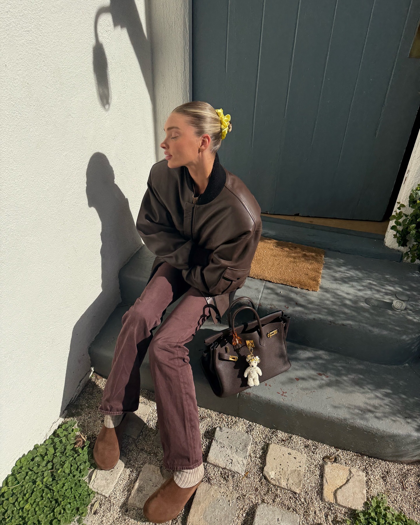 Elsa Hosk wearing a brown leather bomber jacket, brown jeans, and suede clogs