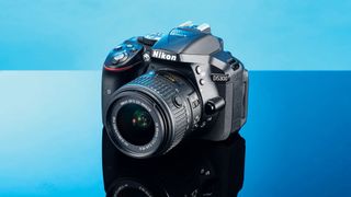 Et Nikon D5300 står på et blankt bord i blåt genskær.