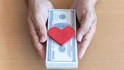 Photo of two hands holding a stack of paper money with a red heart on top