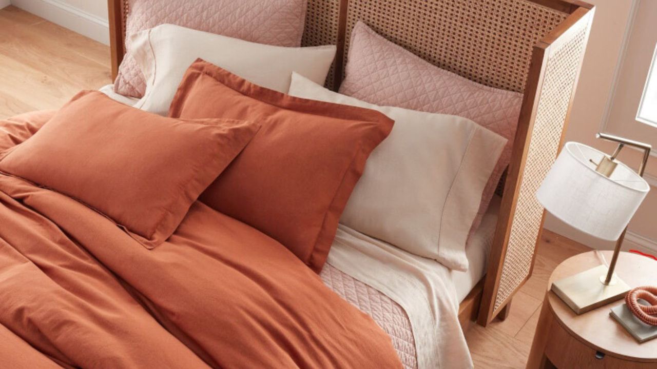 Bird&#039;s eye view of orange, white and pink bedding on a bed against wooden flooring.