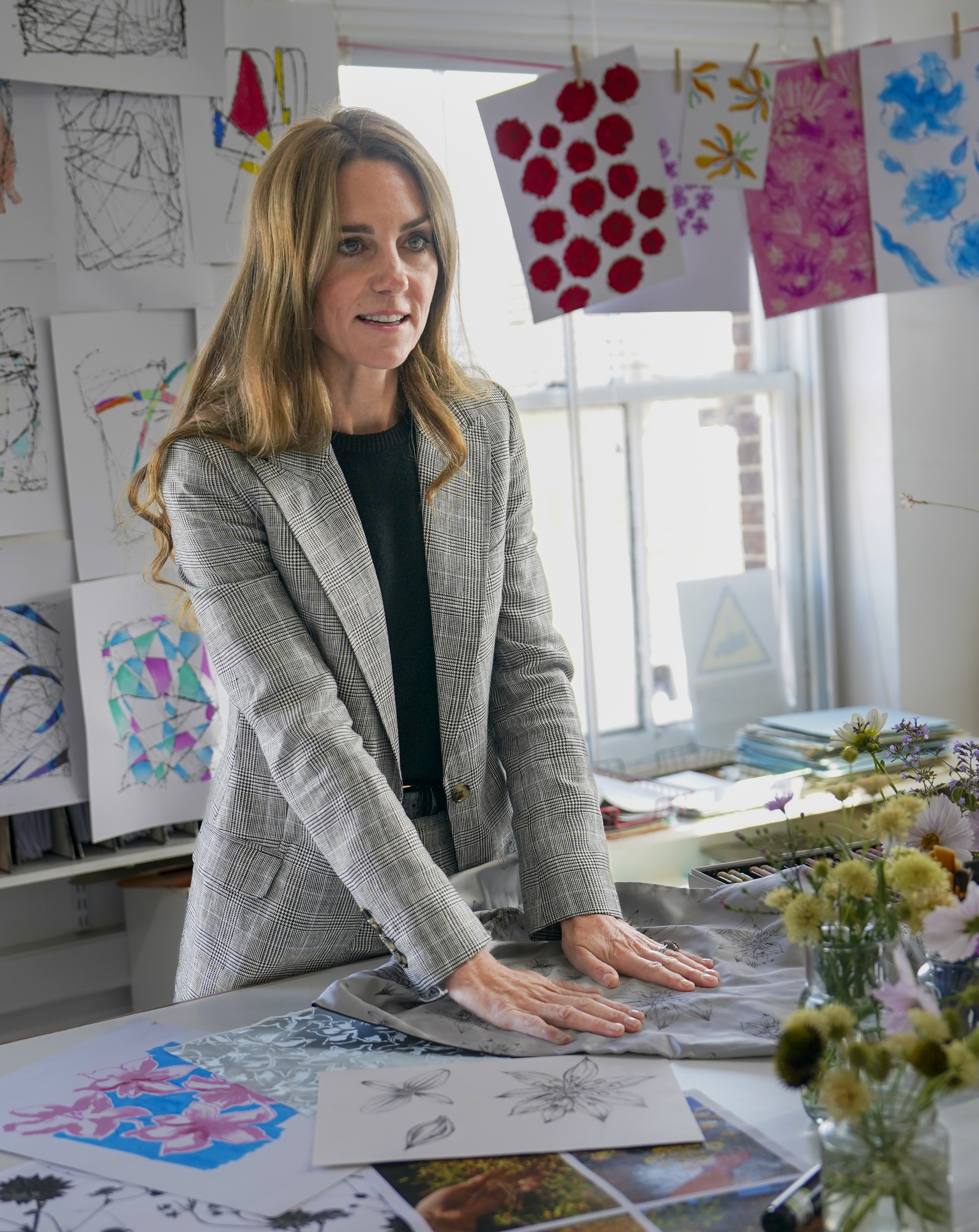 Kate Middleton standing at a table of drawings wearing a gray suit