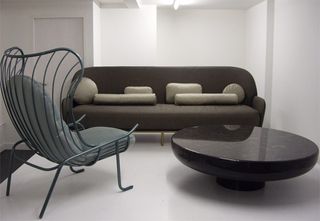 A white room with furniture on display featuring a dark grey sofa with light grey cushions, marble black round coffee table and metal green chair