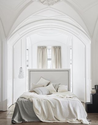 white bedroom with grey and neutral bedding, drapes at window, vaulted ceiling, wooden floors