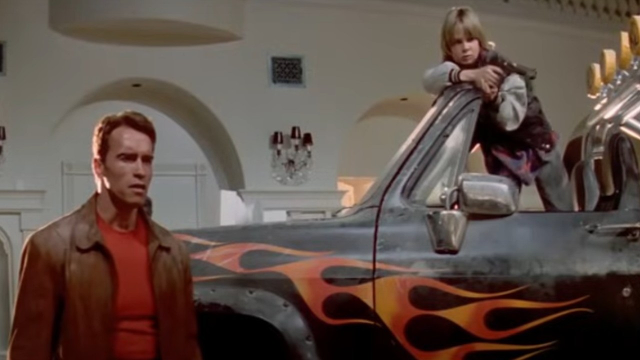 Arnold Schwarzenegger and Austin O'Brien by a car with flames in Last Action Hero