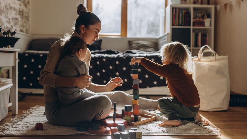 Young Mother playing with children while sitting on floor at home