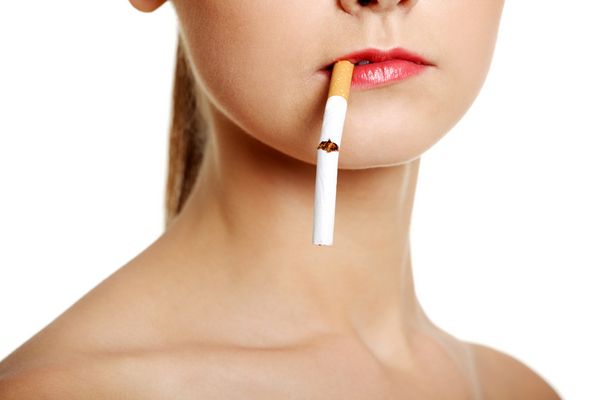 A cigarette, nearly broken in half, dangles from a woman&#039;s mouth. 