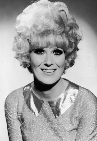 Headshot portrait of Dusty Springfield with dark eye-makeup, a large beehive hairdo, and a sparkling metallic dress