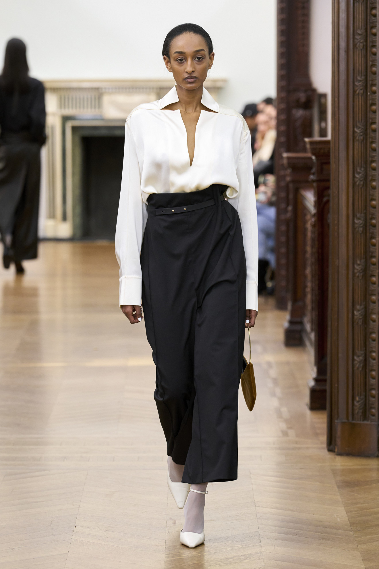 A Bevza model wearing a white blouse and black skirt with white tights and shoes at the F/W 24 show.