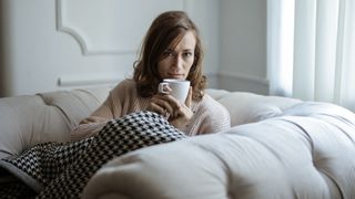 Woman lying on sofa under blanket holding cup