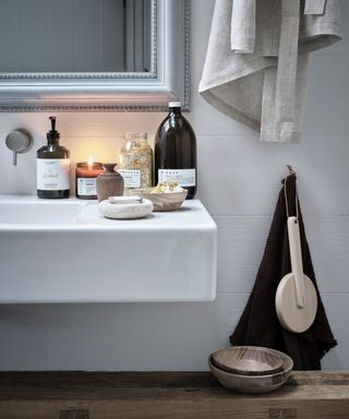 Refined seasonal decor, winter. Detail of amber glass bottles and wooden dishes in bathroom with lit candles