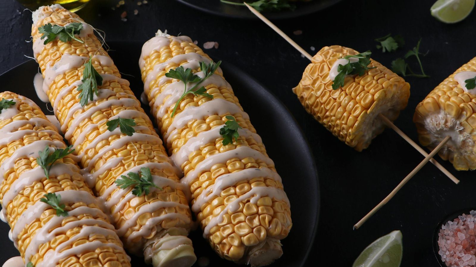 Black ceramic dish of corn on the cob drizzled with a creamy dressing