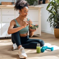 Foods that have more protein than eggs: A woman in gym kit eating a salad and drinking a green juice on her kitchen floor