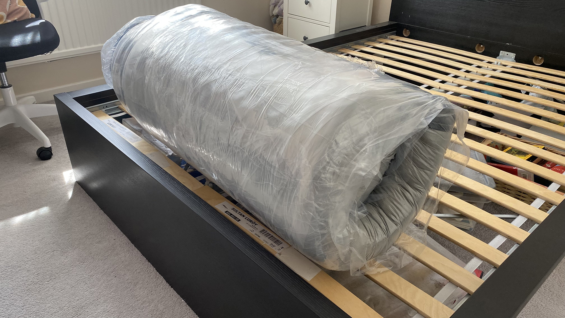 The Dreamstage Value Quilted HYbrid Mattress by Diamond mattress rolled up in its packaging on a bed frame in our reviewer's bedroom