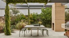 An outdoor garden with a dining space with a green metal set, a fireplace, and an outdoor grill