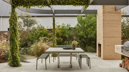 An outdoor garden with a dining space with a green metal set, a fireplace, and an outdoor grill