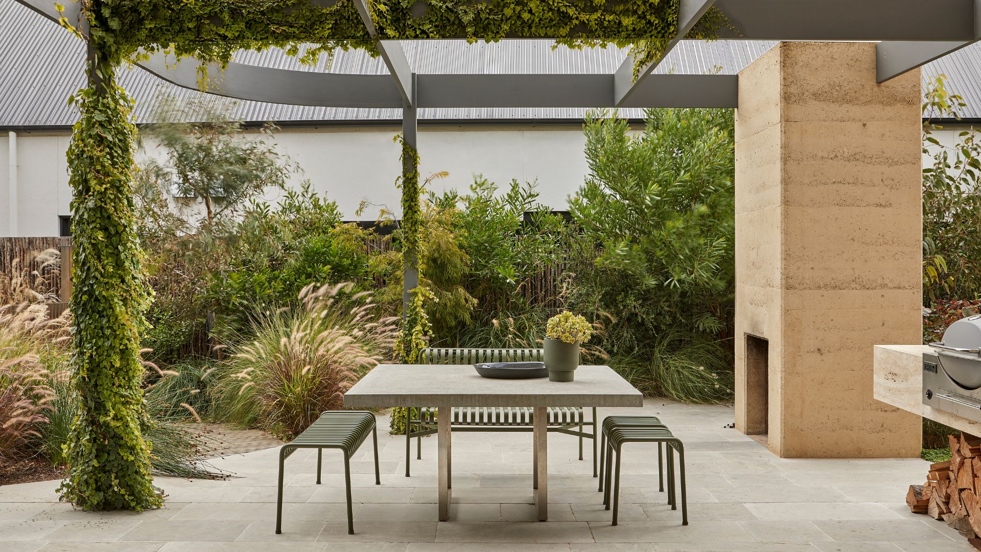 An outdoor garden with a dining space with a green metal set, a fireplace, and an outdoor grill