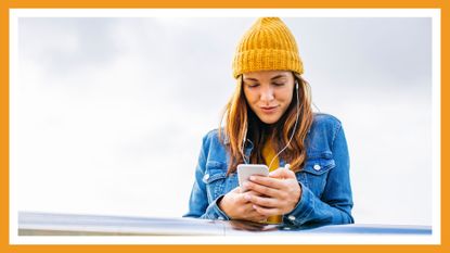 woman on phone in beanie and denim jacket smiling while outside