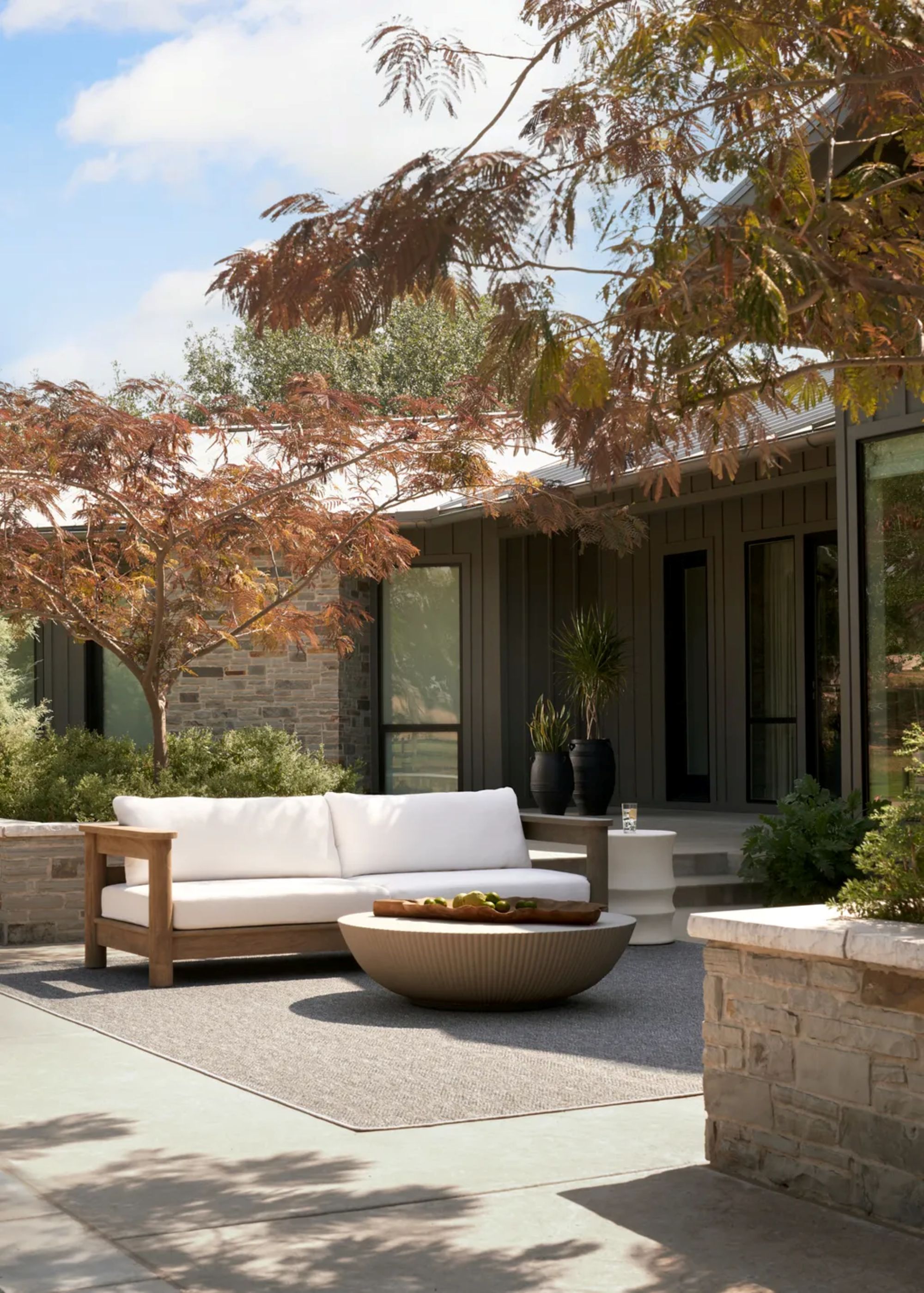 patio area with trees, a wood couch with white cushions, and a round coffee table