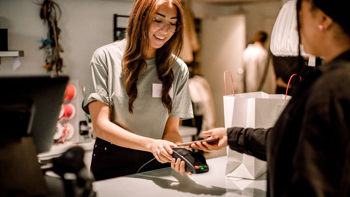 Female customer paying through smart phone to smiling saleswoman at store