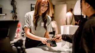 Customer paying through smart phone to smiling saleswoman at store