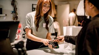 Customer paying through smart phone to smiling sales person at store.