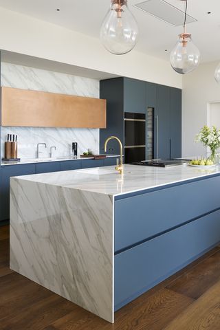 An example of planning a kitchen island, with a long waterfall marble and blue island on a hardwood floor.