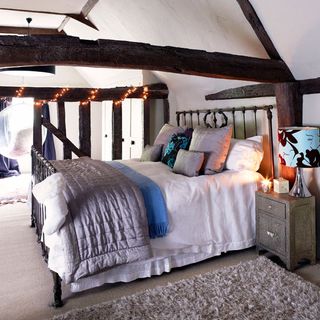 bedroom with white wall and wooden beam and bedding with cushions and throw