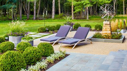 A backyard lounge chairs, bright green plants and mulch 