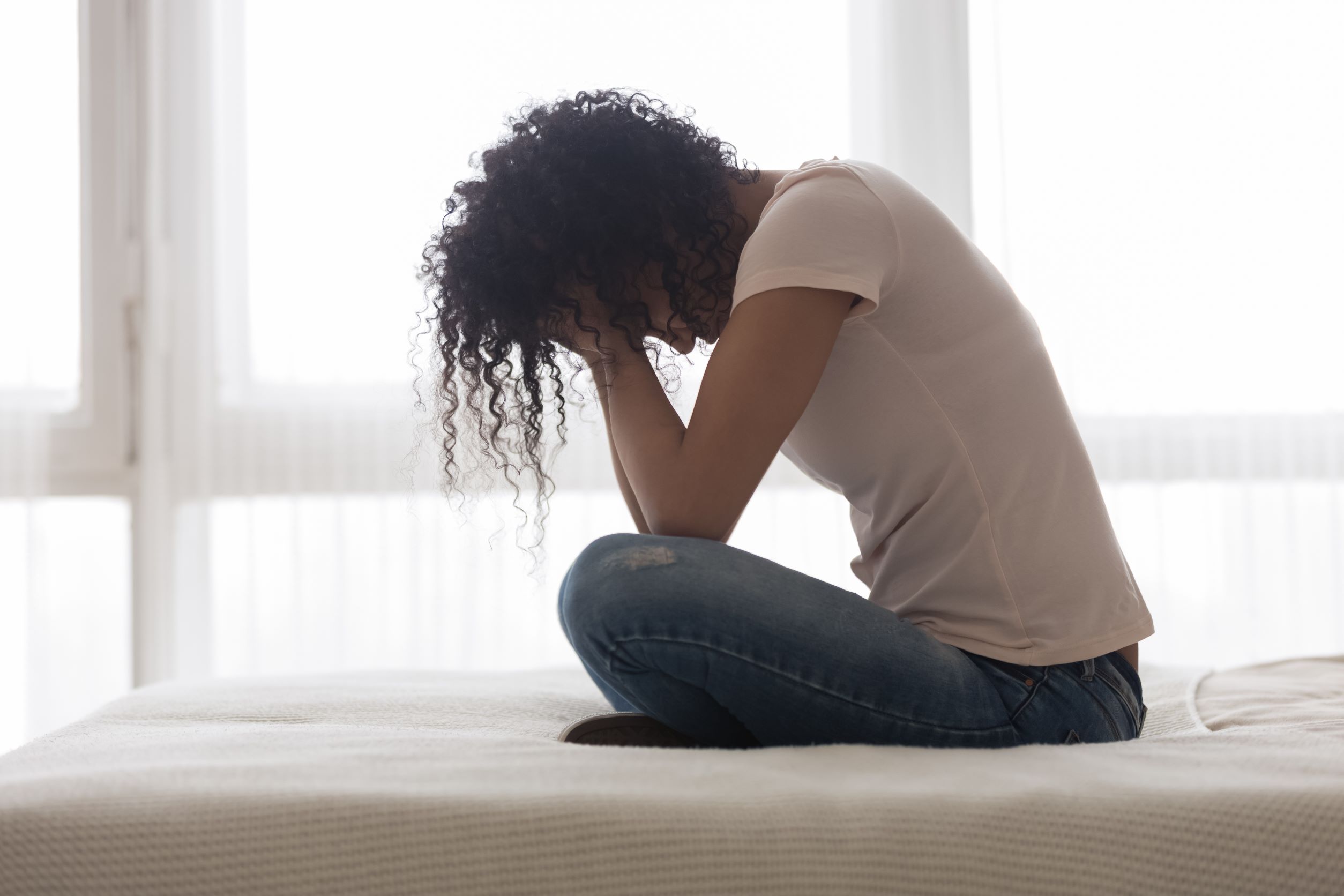 A woman sitting on a bed looking tired and holding her head in her hands.