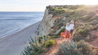 An older couple walk along a bluff at the ocean's edge in Portugal.