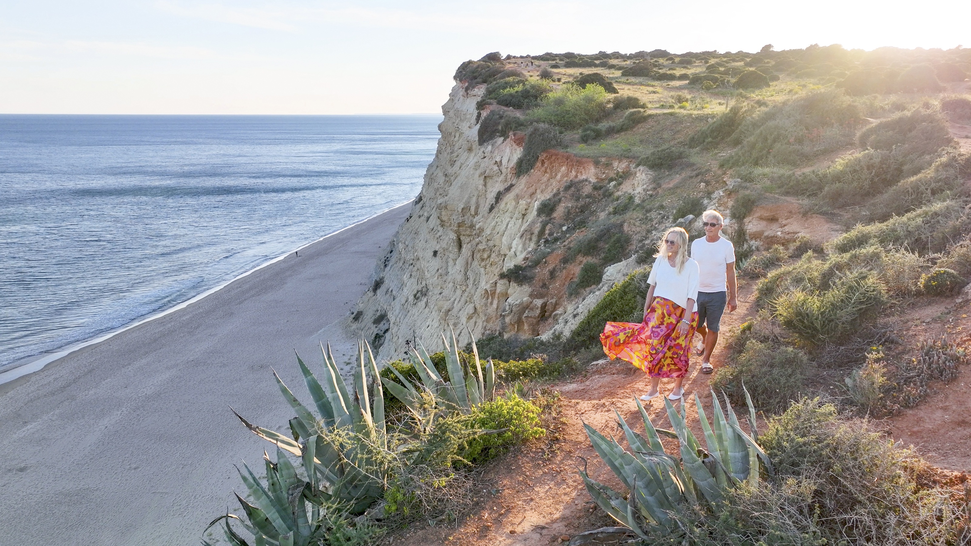 An older couple walk along a bluff at the ocean's edge in Portugal.