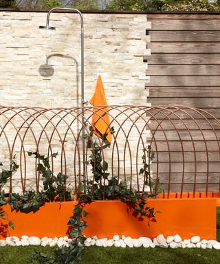 Garden fence decorating ideas with stone and wood behind a bright orange raised bed with brass sculpture.