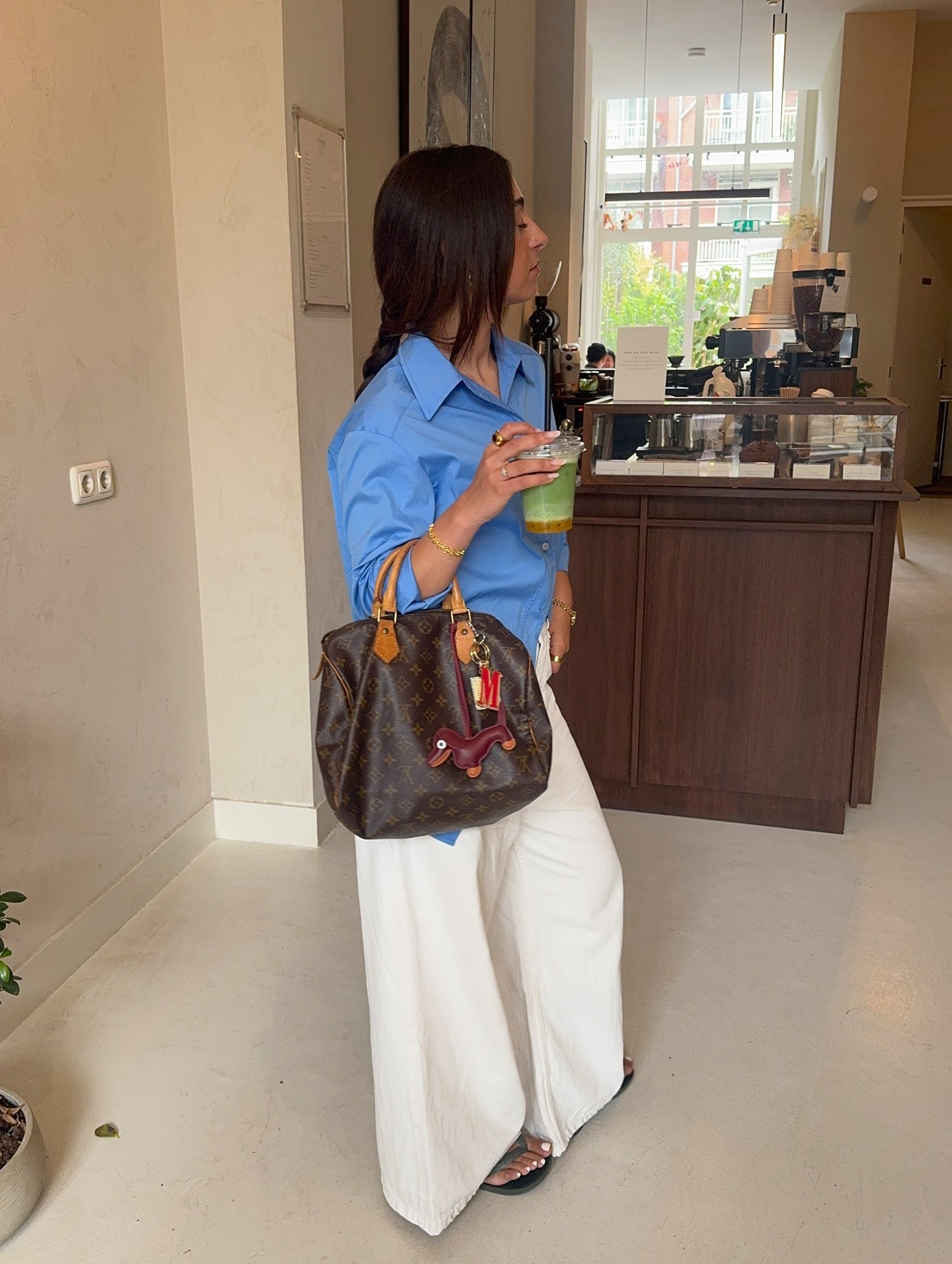 Fashion person Miriam Melenchon wears an olive green sandal,a white denim jacket, a blue shirt and a brown Louis Vuitton speedy bag in a recent image from her Instagram.